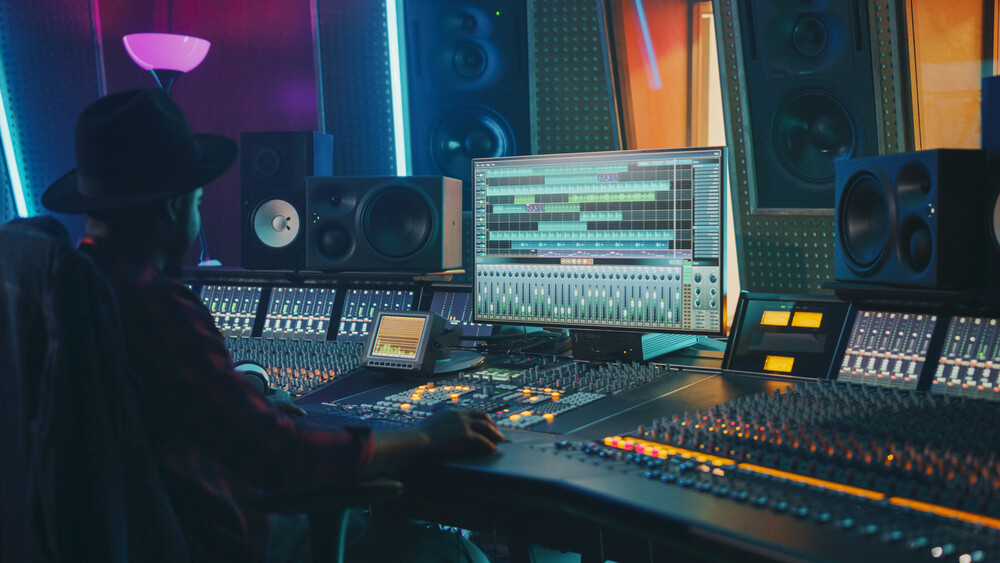 An audio engineer works on a mixing software on his audio console in a dimly lit professional studio